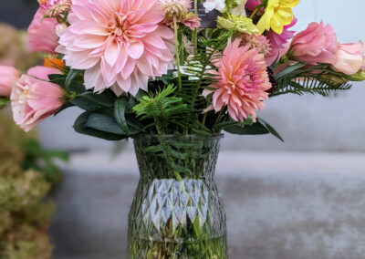 A variety of colorful flowers in a vase on concrete steps of a home.