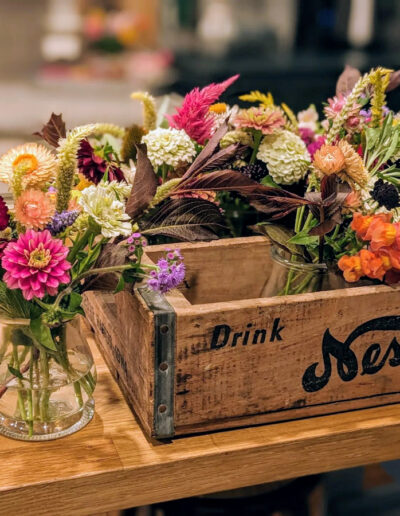 Multiple small floral arrangements in a variety of colors sitting in a vintage wooden box on a counter.