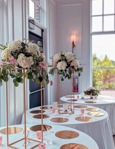 Two white and pink floral arrangements on top of tall holders on tables at a wedding reception.