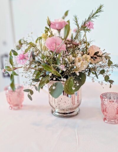 White and pink floral arrangement on a table next to two pink candle holders.