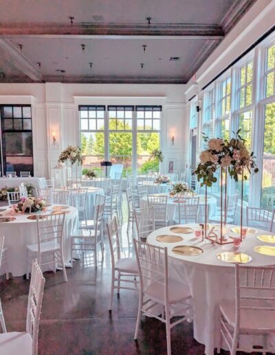 Wedding reception space with white walls, white tables, and white chairs and tall flower arrangements on the circular tables.