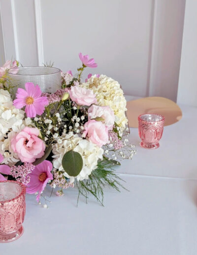 Pink and white flowers on a table next to pink candle holders.