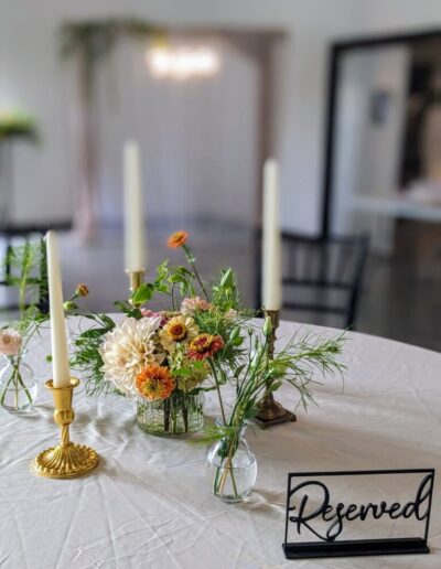 A wedding reception table with a white tablecloth, three candles, and multiple small flower arrangements.