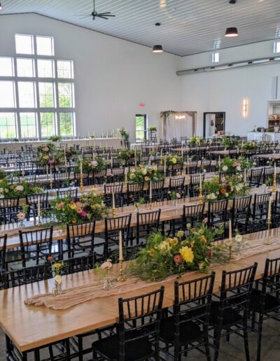 A large event space with several long tables with colorful flower arrangements on them.