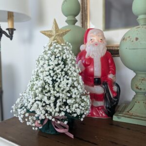 A Christmas tree made of baby's breath next to a Santa ornament on a mantle.